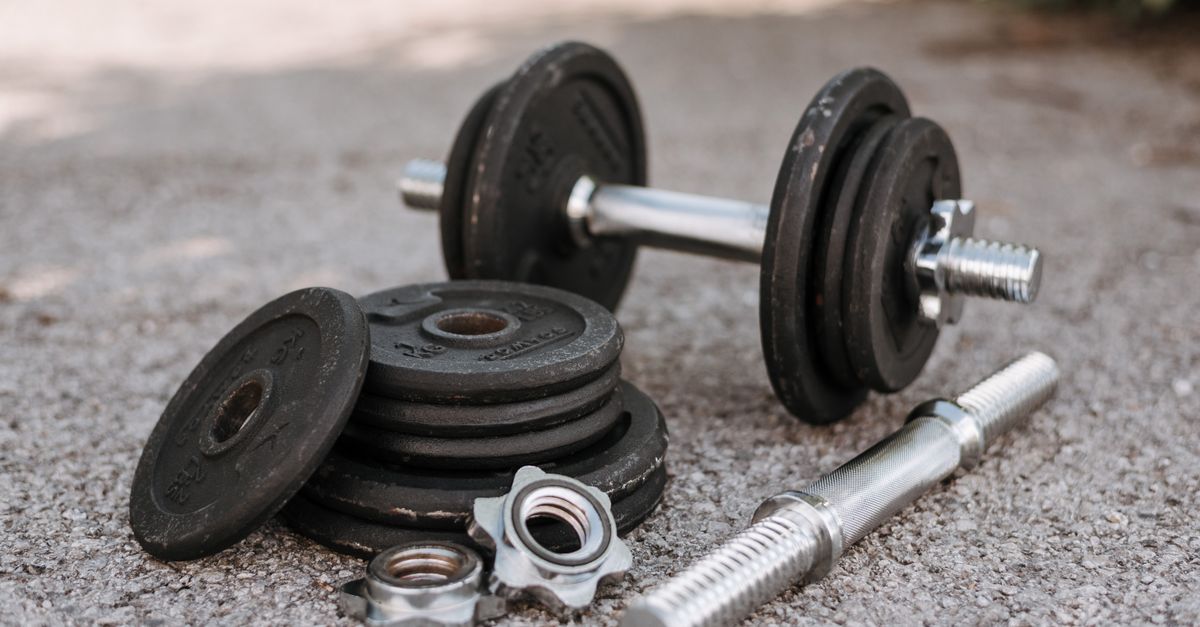 Heavy adjustable dumbbell near cast iron plates and hexagonal collars with stainless steel bar on pavement