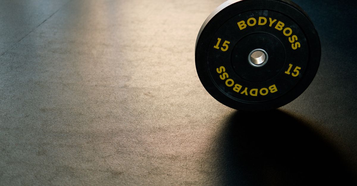 Black BodyBoss weight plate on gym floor, ideal for fitness and workout themes.