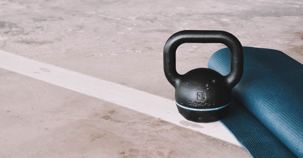 Kettlebell and blue yoga mat on a concrete floor in an indoor gym setting.