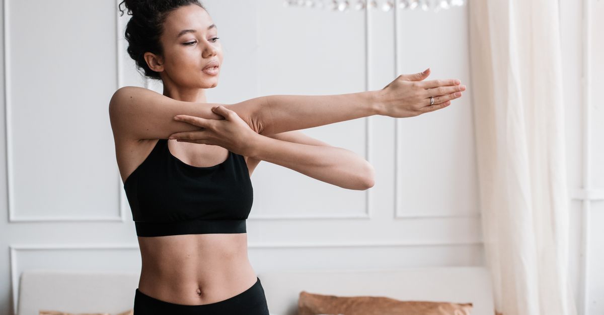 A young woman in activewear stretches indoors, embodying a healthy lifestyle.