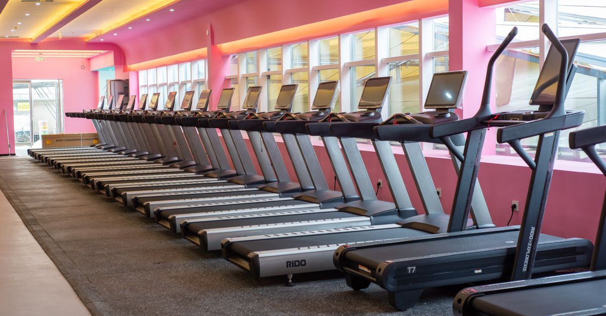 Brightly lit gym with a row of treadmills against a vibrant pink wall, ready for a workout.